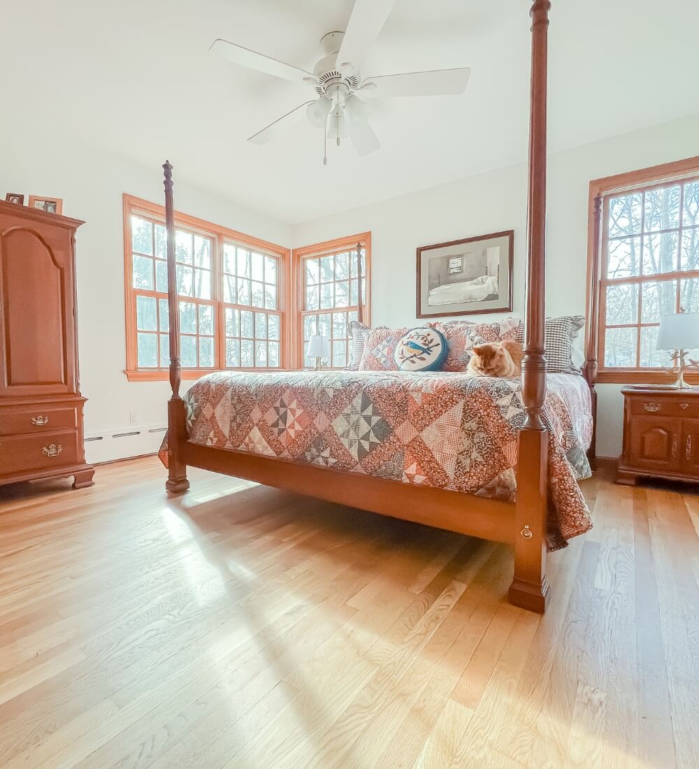 A bright and cozy bedroom with hardwood flooring, a four-poster bed, and large windows letting in ample natural light.