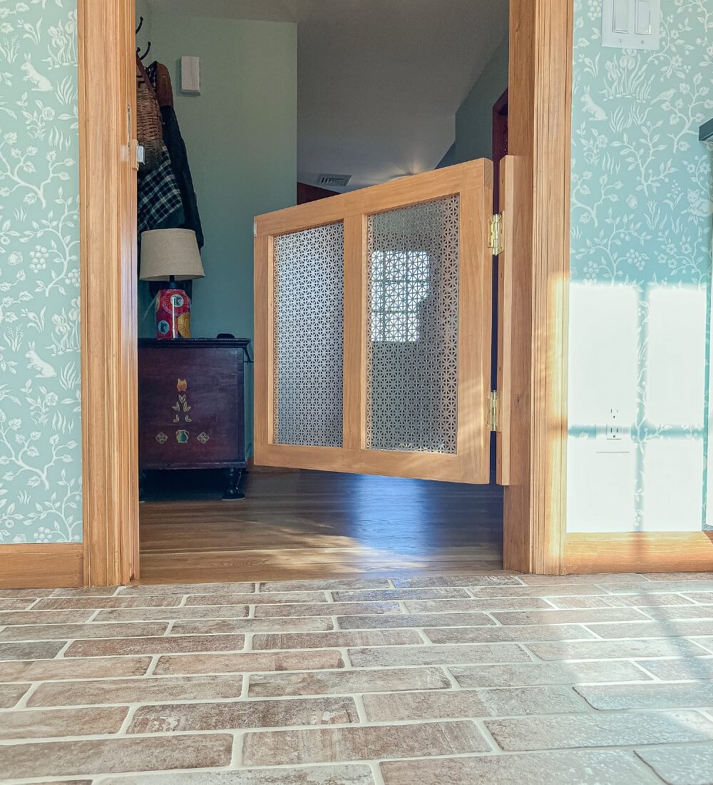 A detailed view of a custom wooden gate with perforated paneling, separating the laundry room and adjacent living space.