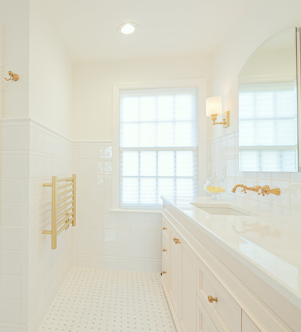 Elegant master bathroom featuring a white double vanity with gold fixtures and a towel warmer under a bright window.