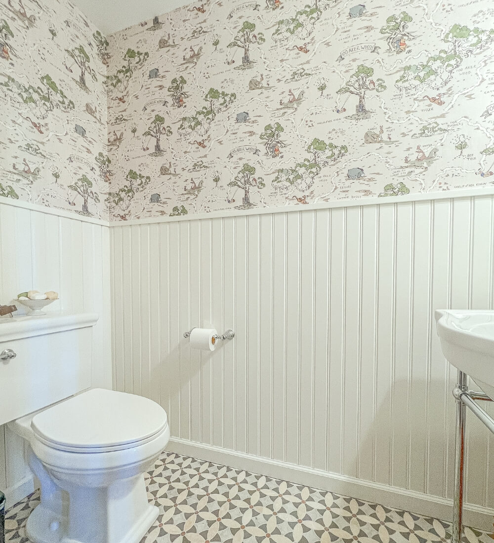 A powder room featuring beadboard wainscoting, a classic toilet, patterned tile floor, and playful wallpaper with nature-themed designs.