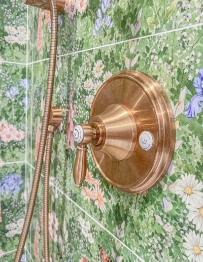 Close-up of a shower with green floral tiles and a luxurious gold shower fixture.