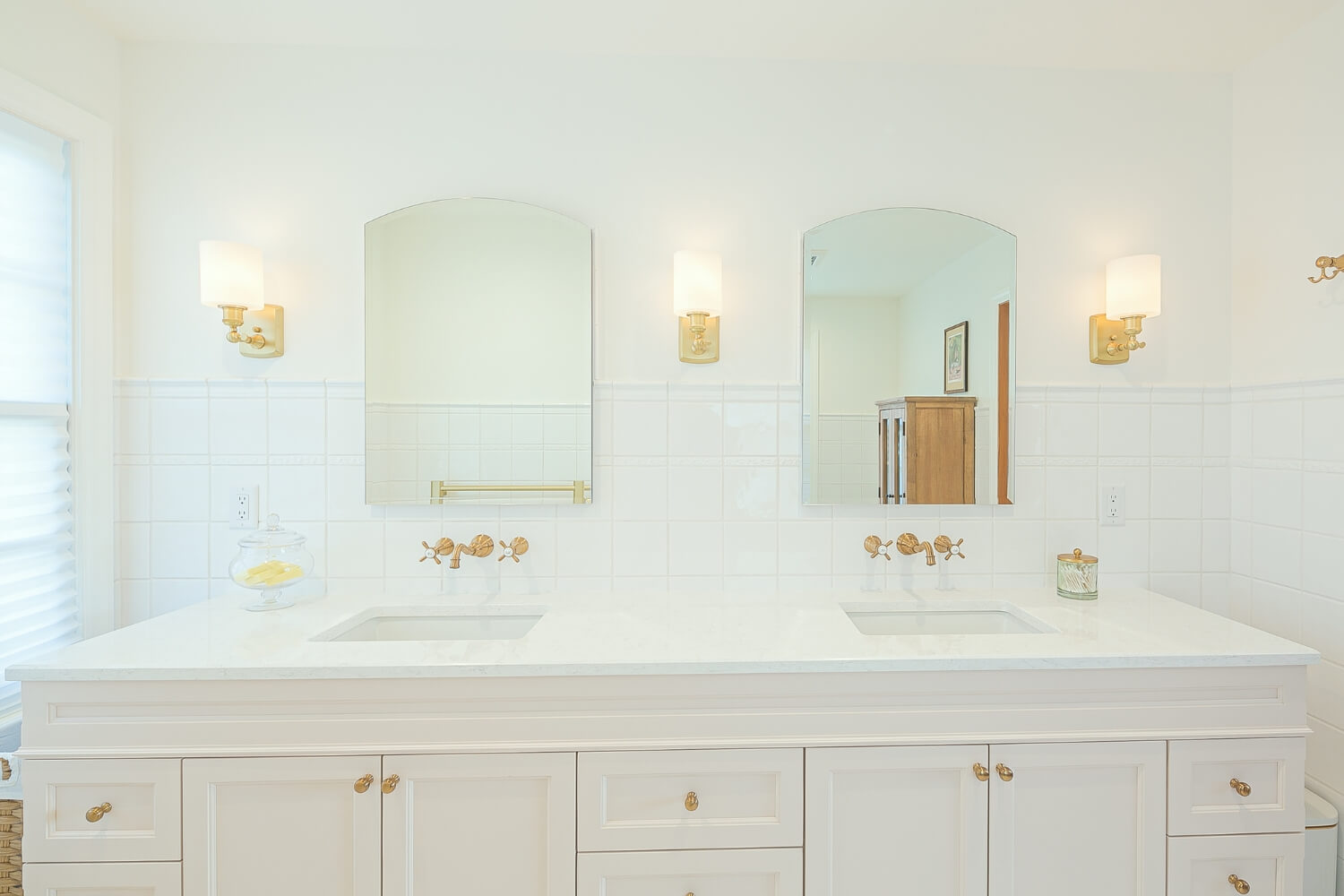 A white double vanity bathroom with brass fixtures and soft lighting.