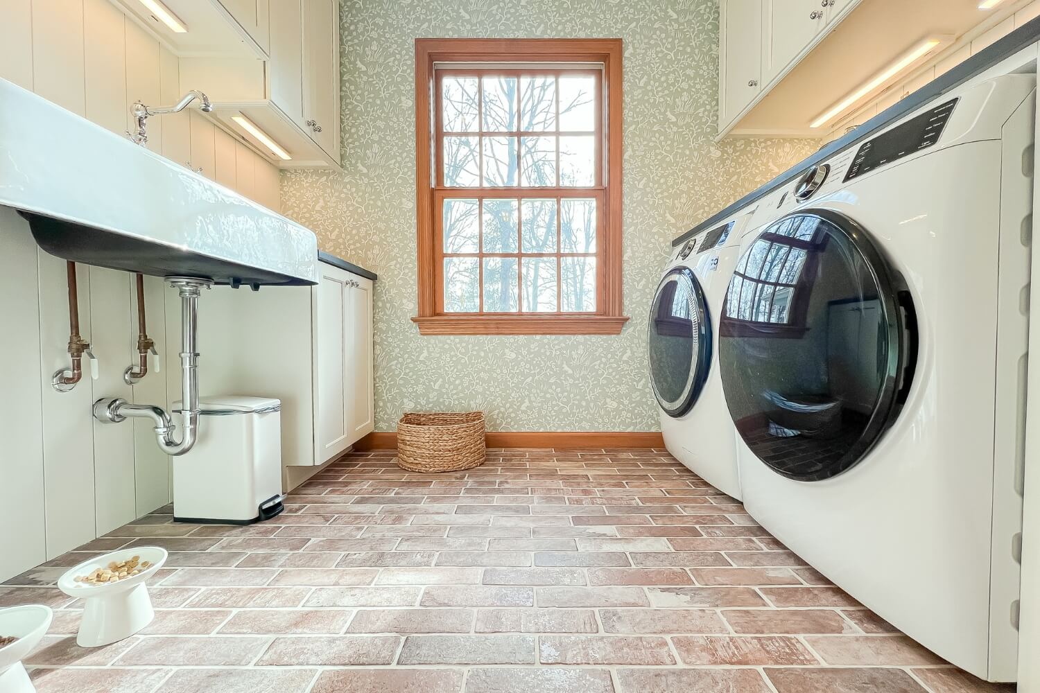 Bright laundry room with a large window, farmhouse sink, and patterned wallpaper.