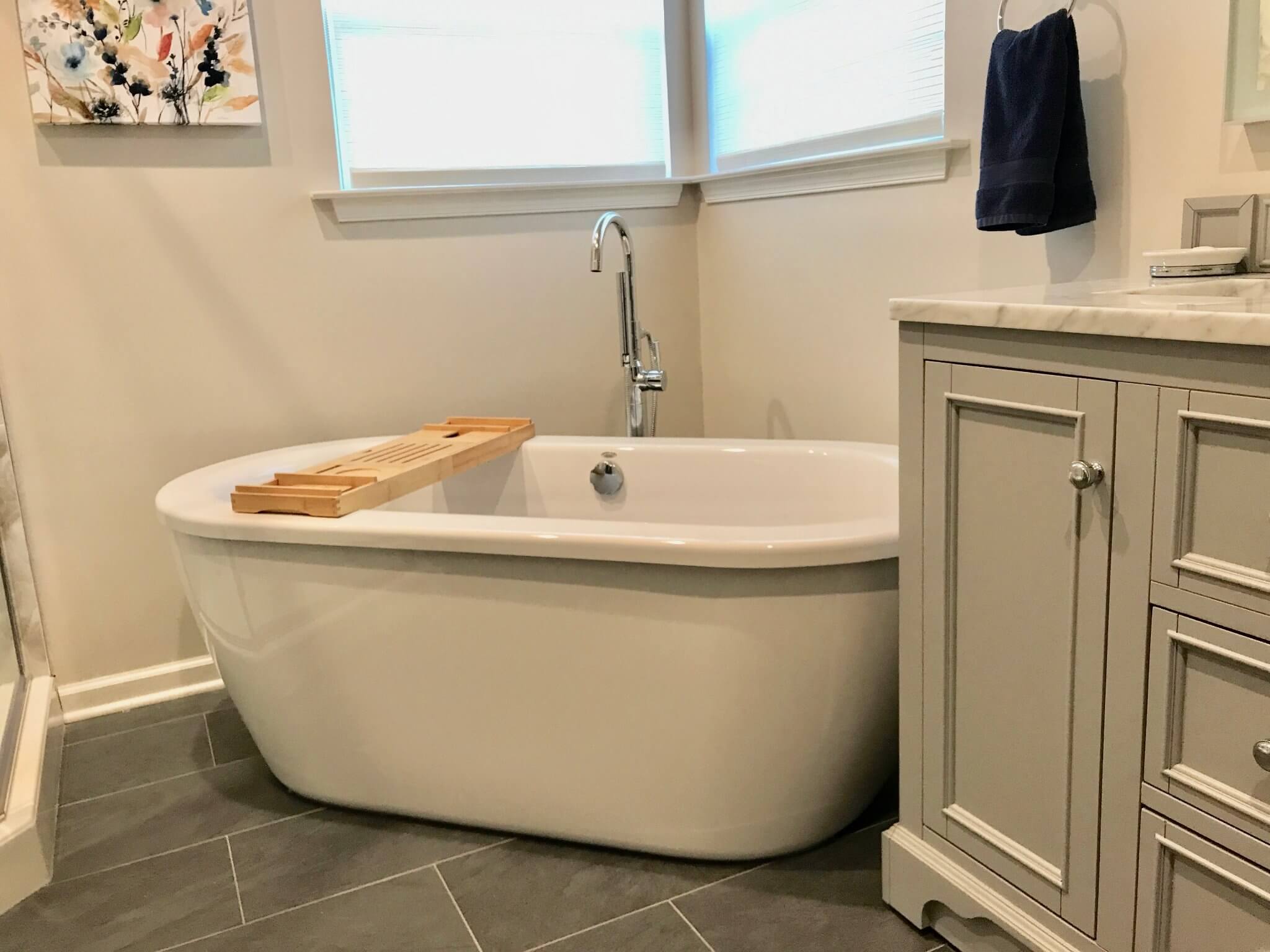 White freestanding bathtub with a wooden bath tray in a spa-like bathroom.